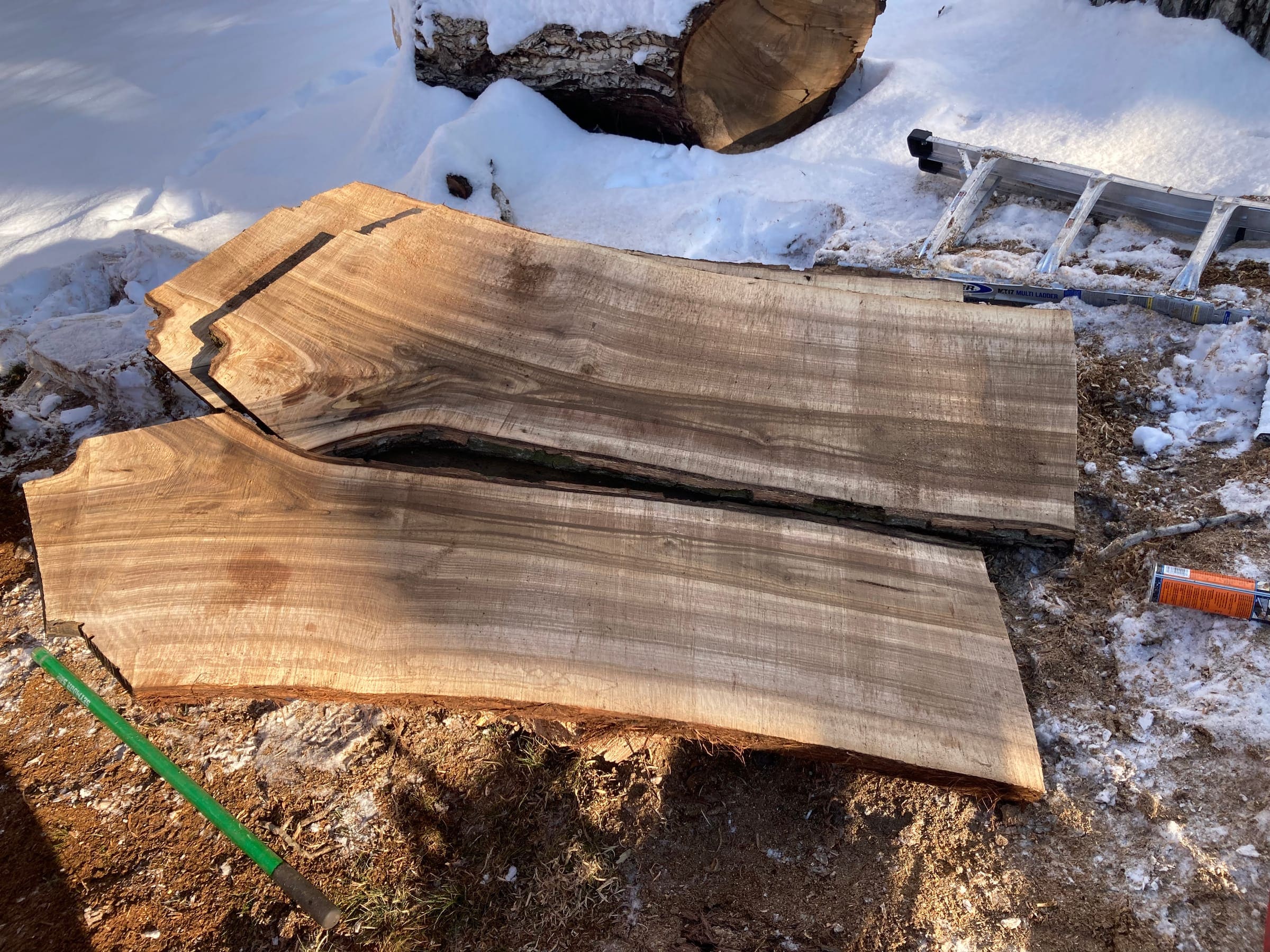 Two freshly milled wood slabs on the snow beside the log they were cut from